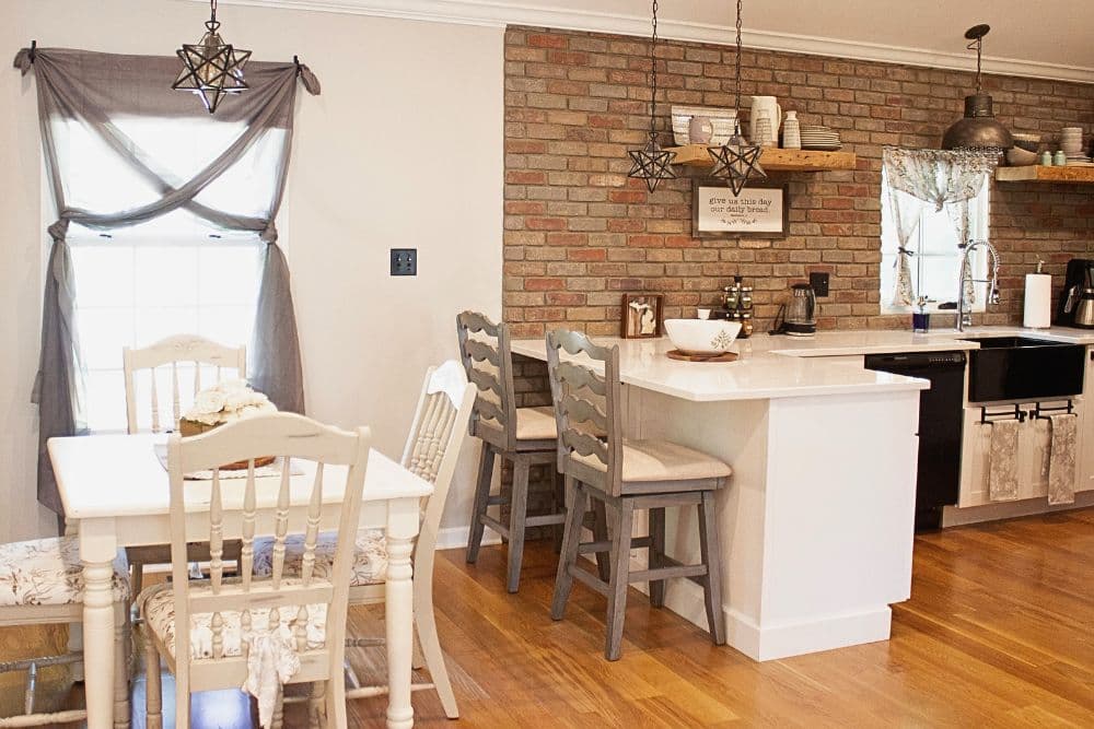 Bright kitchen with a brick accent wall, white cabinets, and a dining area featuring a table and chairs.
