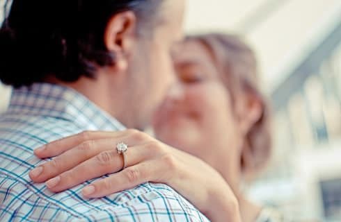 A close-up of a couple embracing, showcasing an engagement ring on the woman's hand.