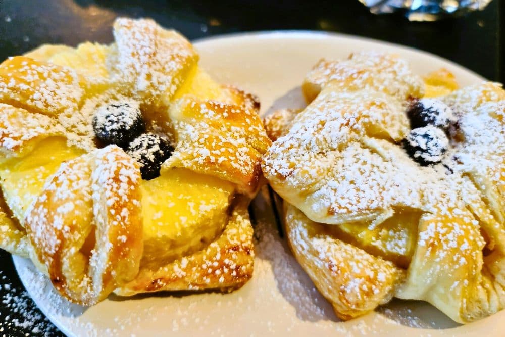 Two flower-shaped pastries dusted with powdered sugar and topped with a dark berry.