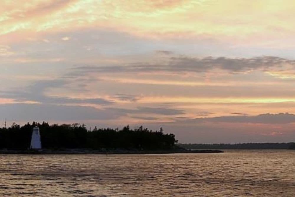 A tranquil sunset over water with a lighthouse on the shore.