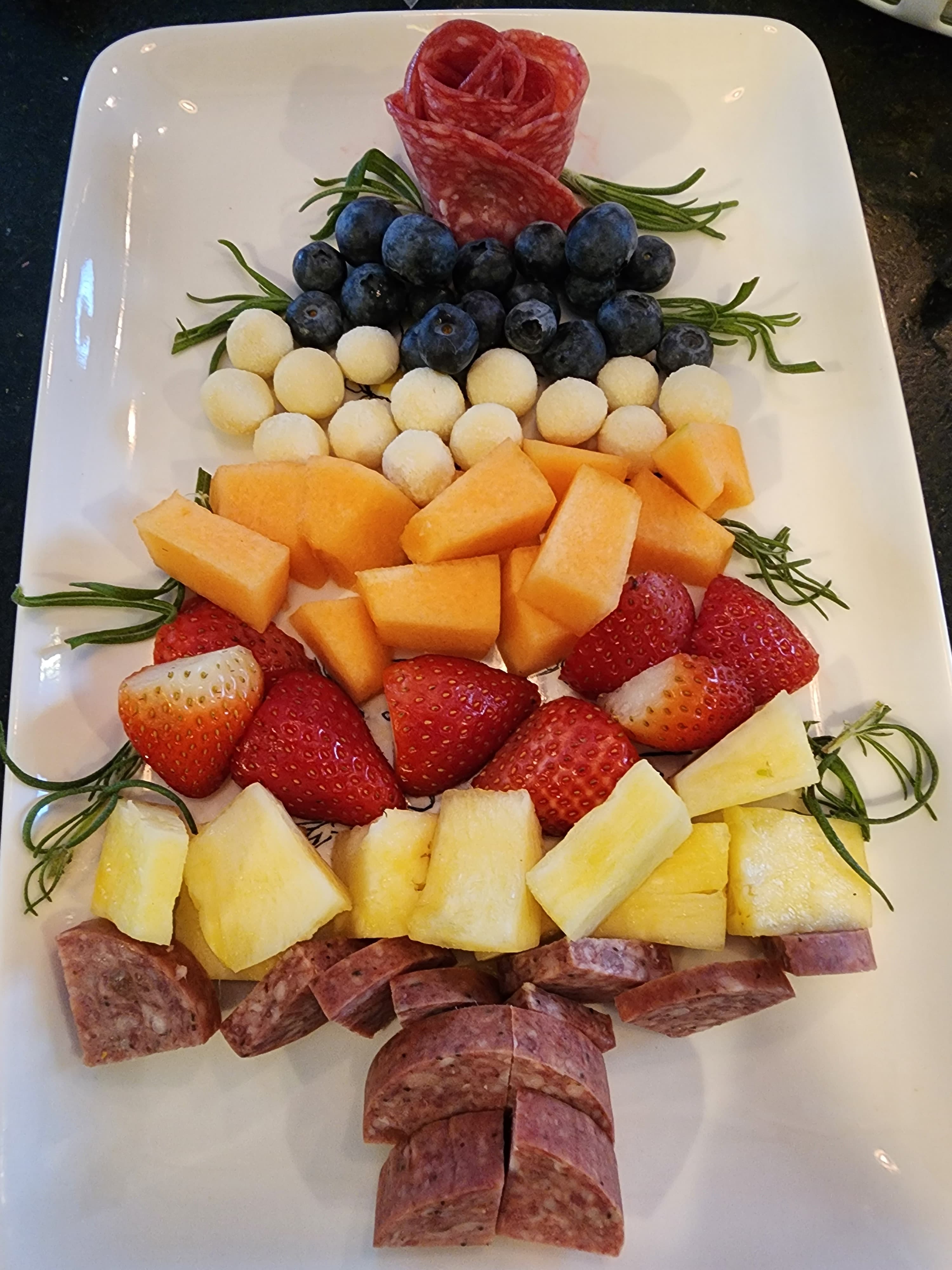 A festive platter arranged like a Christmas tree, featuring assorted fruits and meats.