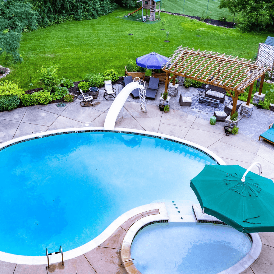 Aerial view of a landscaped backyard featuring a swimming pool with a slide, a hot tub, and a shaded seating area.