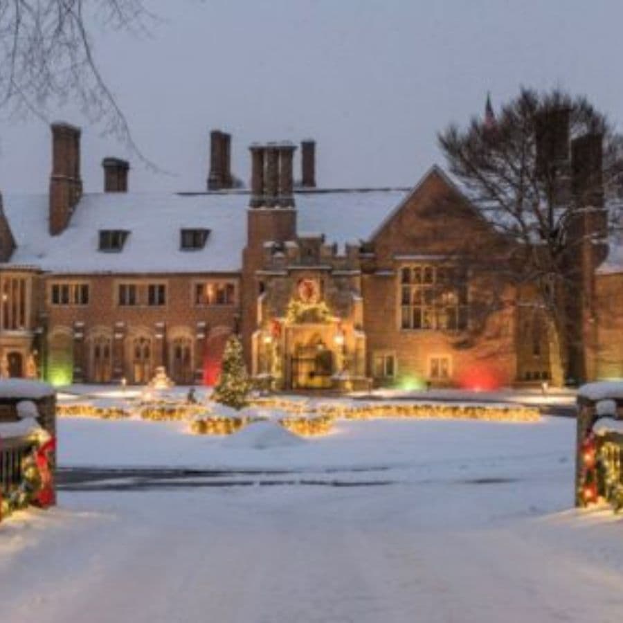 A grand, snow-covered mansion beautifully decorated with festive lights and holiday greenery.