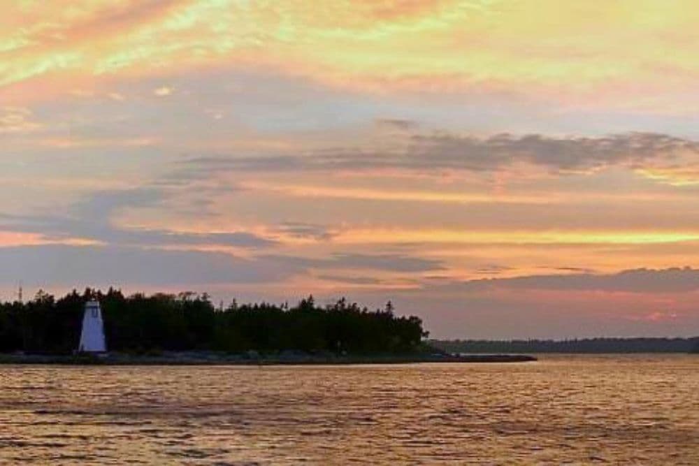 A picturesque sunset over water with a lighthouse on a distant shore.