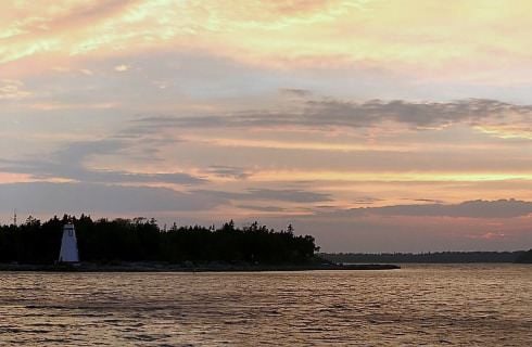 Small island with small white lighthouse and trees surrounded by water at dusk