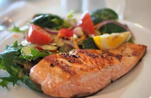 Close up view of fried salmon next to a fresh salad on a white plate