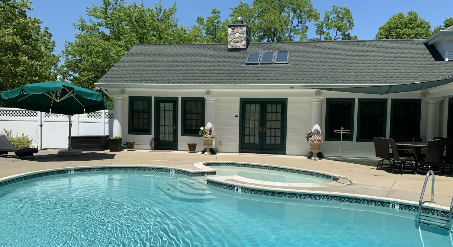 Exterior view of the property painted white with dark trim next to a large swimming pool with hot tub