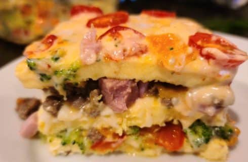 Close up view of egg casserole lasagna with cheese, ham, tomatoes, and broccoli