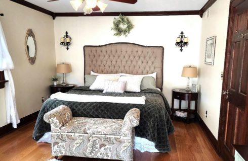 Bedroom with white walls, hardwood flooring, upholstered headboard, gray bedding, and dark wooden nightstands with lamps