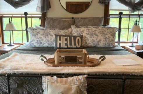 Bedroom with wrought iron bed, gray bedding, wooden nightstands with lamps, and windows with views to the outside