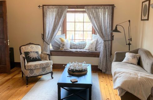 Room with a multicolored upholstered armchair, gray upholstered chair and loveseat, and dark wooden coffee table next to a bay window