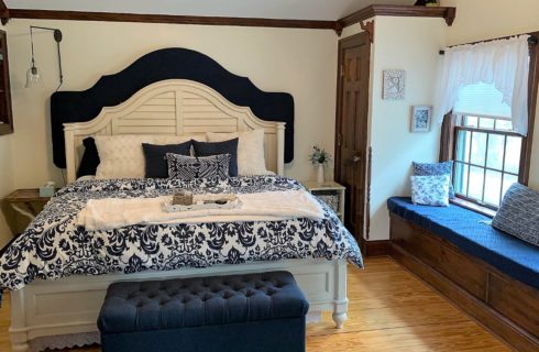 Bedroom with white walls, hardwood flooring, white wooden bed, navy and white bedding, and long window seat with blue cushion