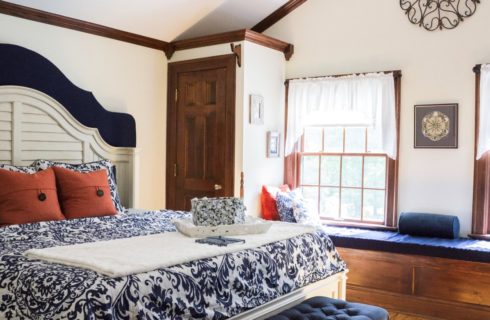 Bedroom with white walls, hardwood flooring, white wooden bed, navy and white bedding, and long window seat with blue cushion