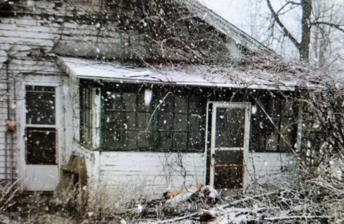 Dilapidated white house covered in dead branches and falling snow