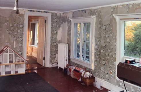 Living room with damaged wallpaper, hardwood flooring, and old belongings
