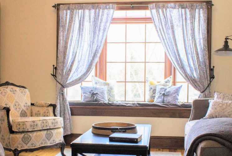 Room with a multicolored upholstered armchair, gray upholstered chair and loveseat, and dark wooden coffee table next to a bay window