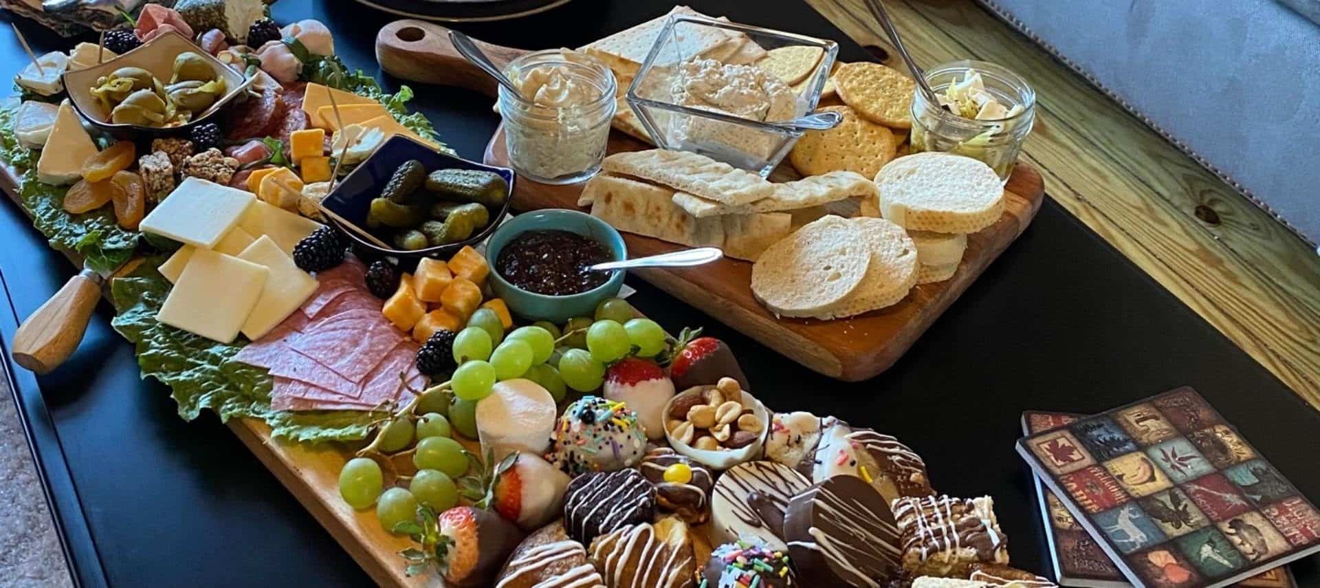 Large charcuterie boards filled with desserts, fruit, cheese, meat, pickles, crackers, and breads