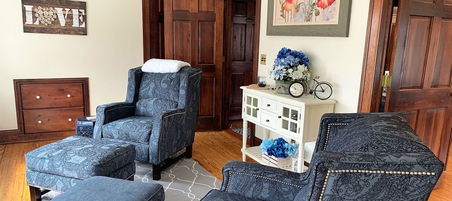 Two paisley blue upholstered armchairs with ottomans in a room with white walls and hardwood flooring