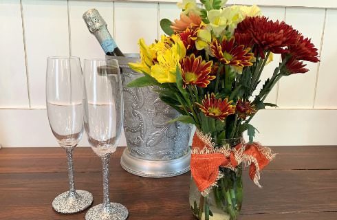 Two Champagne flutes, silver ice bucket, and vase of flowers on dark wooden table