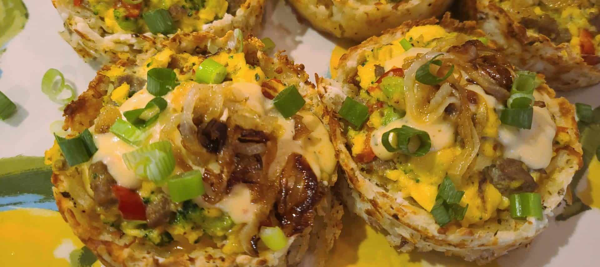 Close up view of hashbrown cups filled with eggs, cheese, sausage and onions