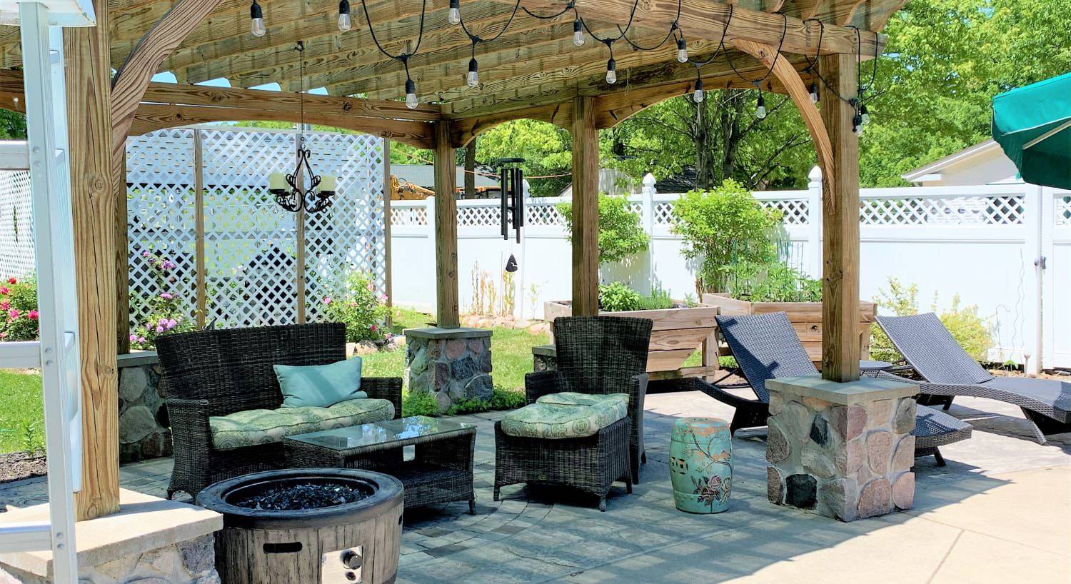 Large concrete patio covered by a wooden pergola with brown wicker patio furniture and fire pit